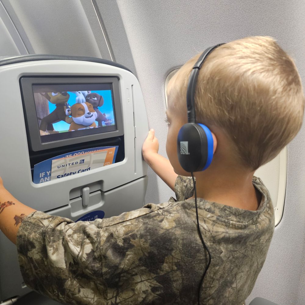 A toddler in an watching Paw Patrol on a seatback television 