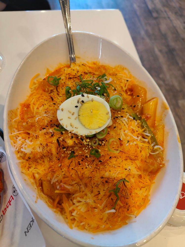 Rosé tteokbokki with cheese, fish cakes, and an egg on top served in a dish