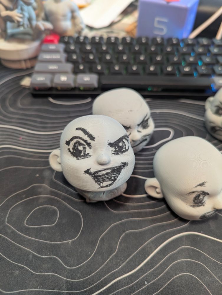 Several 3d printed Customizable blank Designer Art Toys with a range of facial expressions drawn on with charcoal pencil.   Front one has an excited mischievous smile