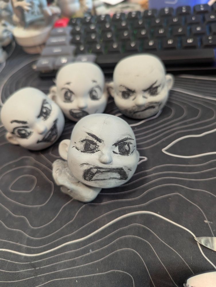 Several 3d printed Customizable blank Designer Art Toys with a range of facial expressions drawn on with charcoal pencil.   Front one has an angry look