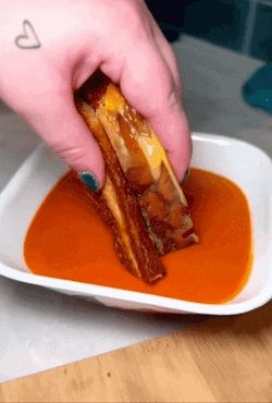 a person is dipping a grilled cheese sandwich in a bowl of sauce