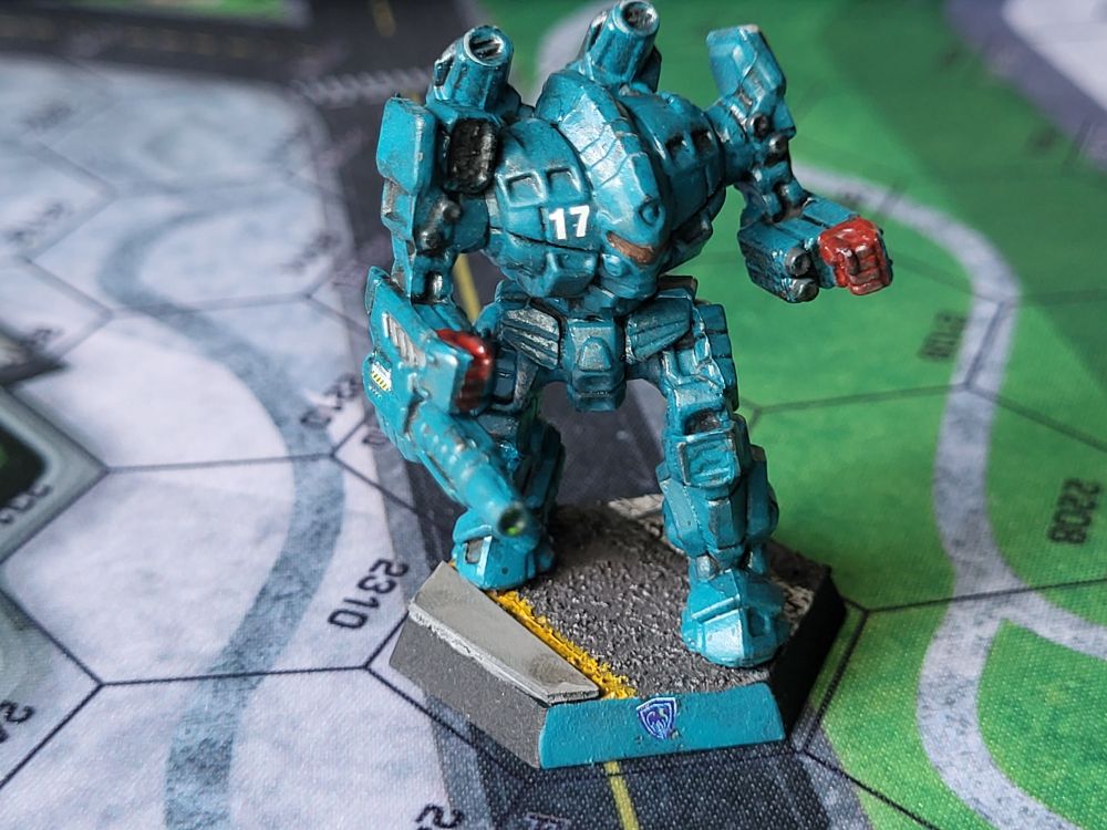 A teal blue Guillotine battlemech stands on a city street, ready for combat. It's hands are painted red in remembrance of the blood shed for Rasalhague independence. The number 17 is painted in white on its chest. (Painted miniatures)