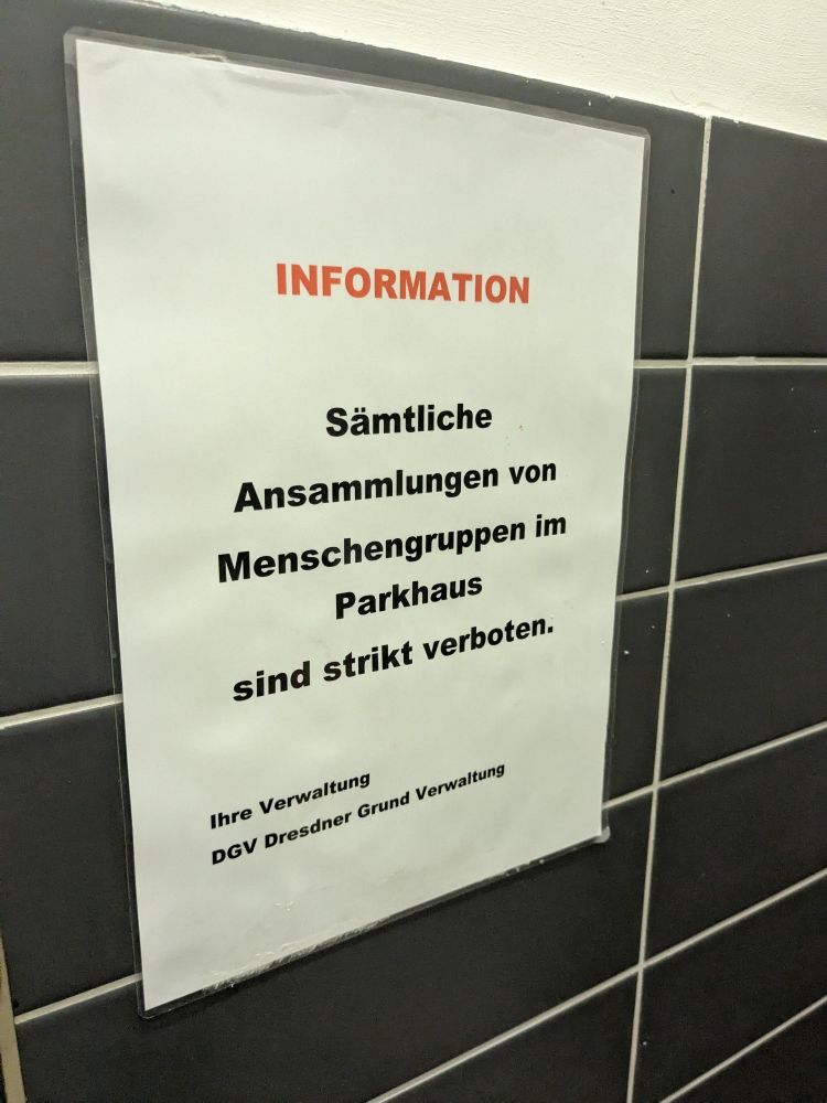 Infoblatt an einer gefliesten Wand mit der Aufschrift: "Information: Sämtliche Ansammlungen von Menschengruppen im Parkhaus sind strikt verboten. Ihre Verwaltung DGV, Dresdner Grund Verwaltung" 
