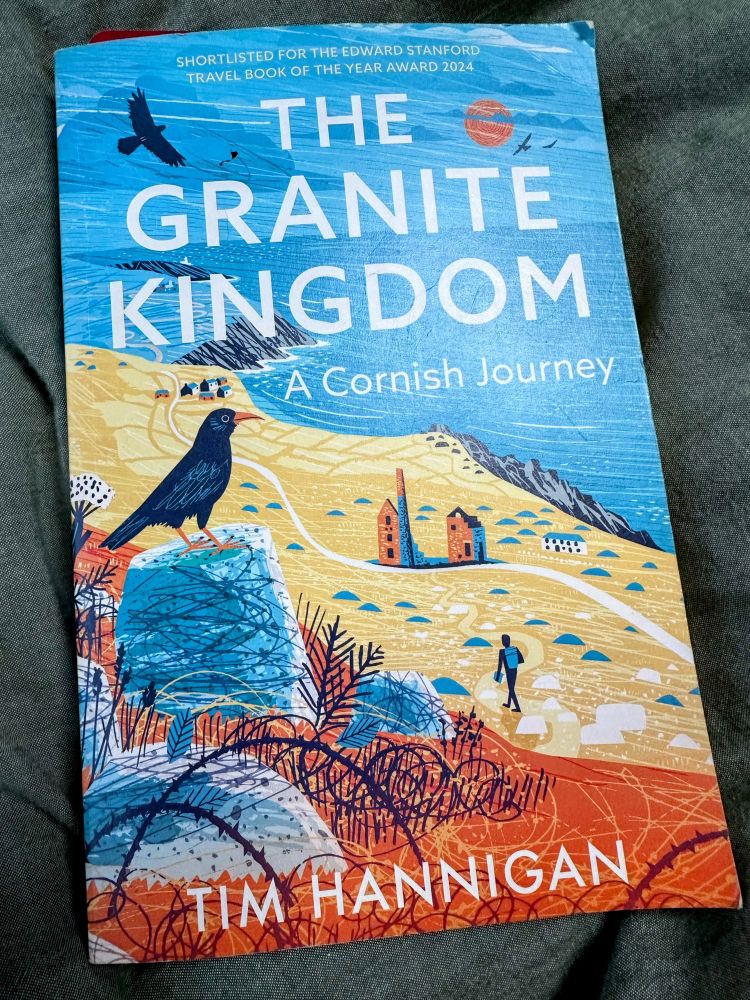 The cover of a book, The Granite Kingdom: A Cornish Journey by Tim Hannigan, shows a hiker in a tin mining landscape by the coast, with a Cornish Chough looking down from high rocks.