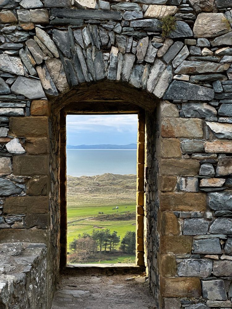 A view through a doorway at Harlech Castle reveals sand dunes and sea beyond.