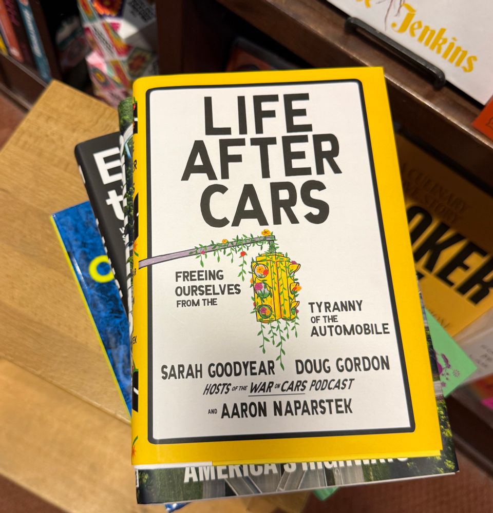 A photo of a stack of books in a bookstore sitting on a wooden step stool, with the book “Life after Cars” on top 