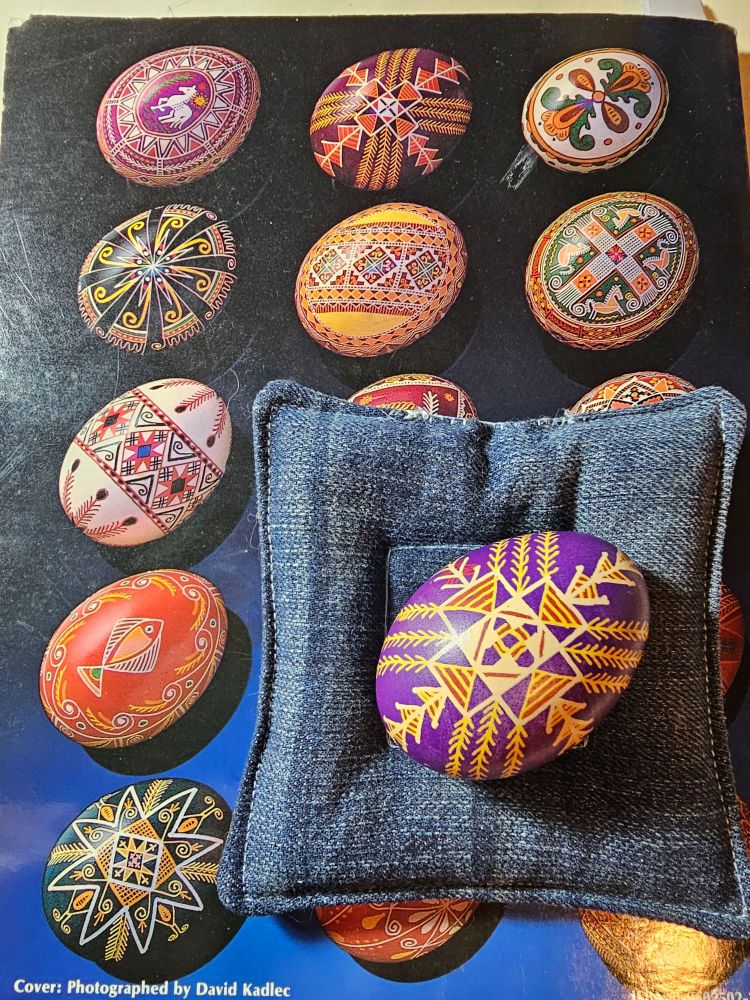 Ukrainian Design Book 1, Pysanka 2 sitting on a blue denim cushion, on top of the book. 