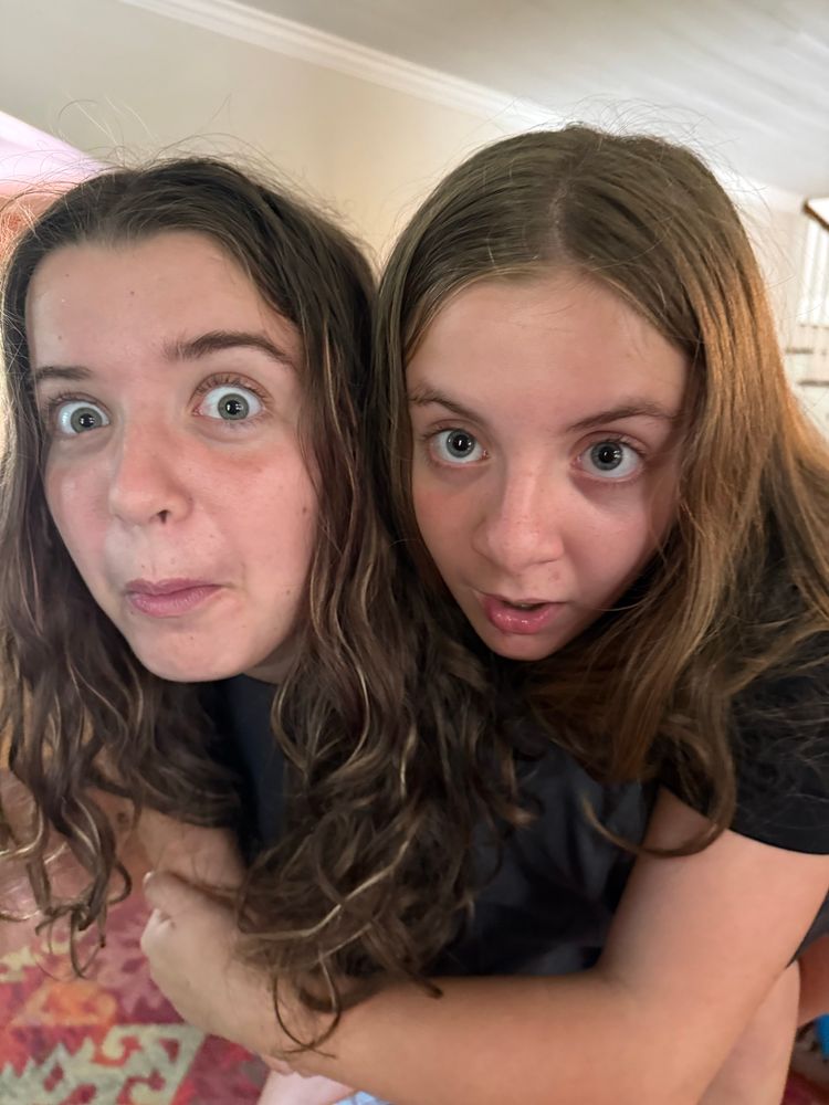 2 white children with long wavy brown hair and staring with wide eyes into the camera, heads next to each other