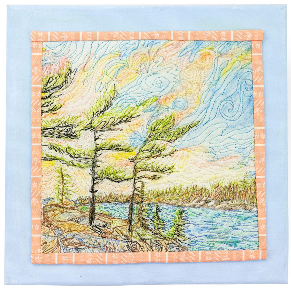 A fibre art depiction of windswept pine trees beside a blue lake.