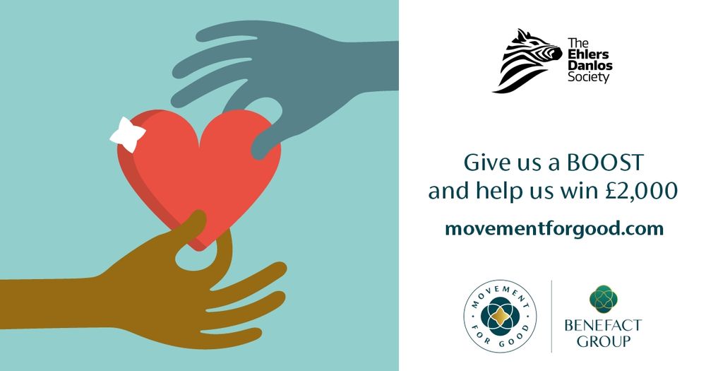 A promotional graphic for The Ehlers-Danlos Society features an illustration of two hands exchanging a red heart. One hand is dark brown and reaches from the bottom, while the other is dark blue and reaches from the top. The heart has a small white plaster on it. On the right side, the text reads: “Give us a BOOST and help us win £2,000” followed by the website “movementforgood.com.” The Ehlers-Danlos Society logo with a zebra head is displayed above the text. At the bottom are the logos for "Movement for Good" and "Benefact Group."
