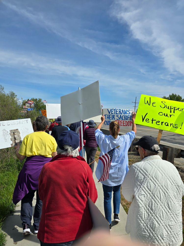 A line of protest marchers. One sign reads "We Support our Veterans!"