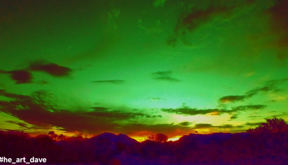 Stylized photograph, the color inversion of a sunset behind a mountain with a green sky.