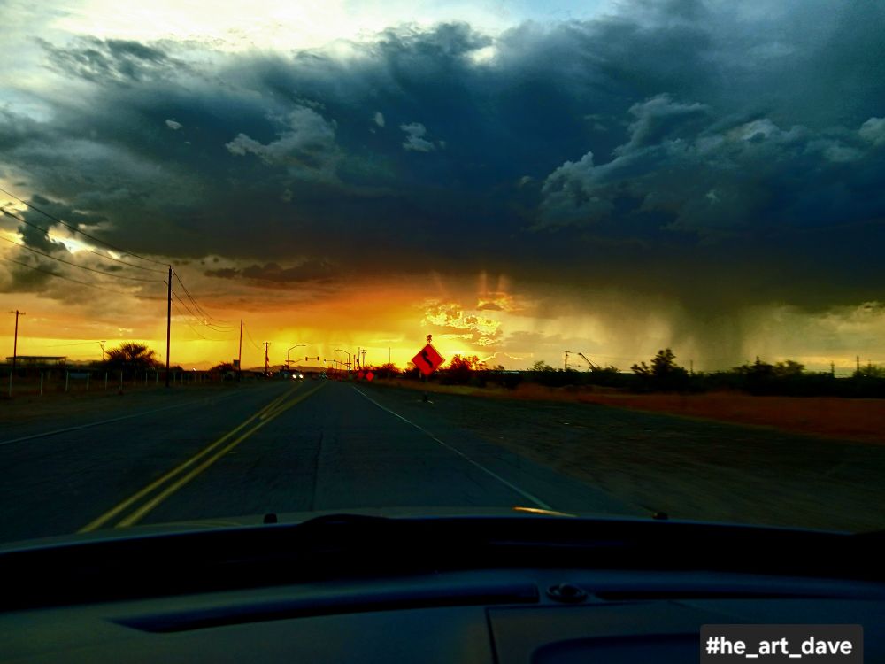 A desert highway from inside a car, a monsoon storm looms in the distance. 