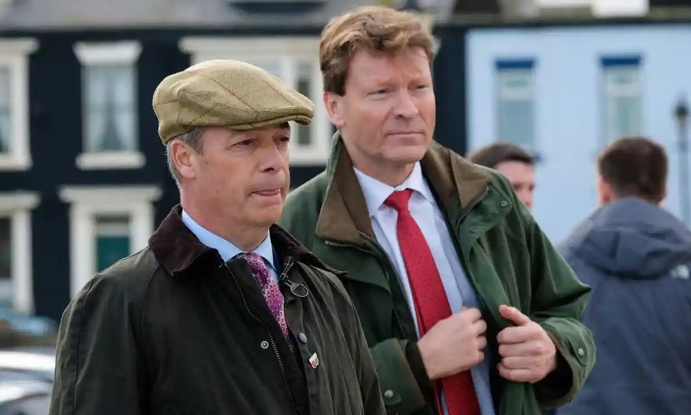 Farage in flat cap & waxproof jacket alongside Tice also wearing a waxproof jacket.