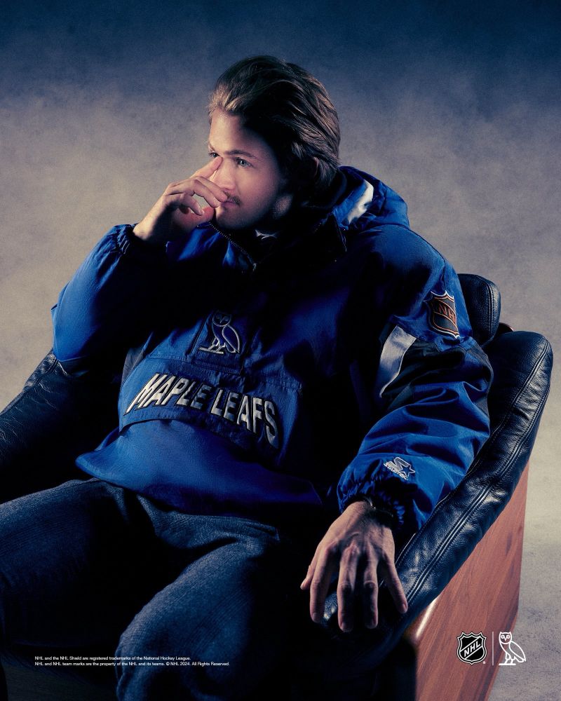 William Nylander in the new “All Canadian” OVO x Maple Leafs Winter collection photo shoot. Wearing a blue starter jacket with the OVO owl logo and Maple Leafs in white text. He’s sitting in a black and brown arm chair