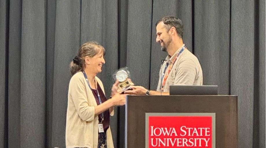 A woman accepts an award from a man standing behind a lectern reading Iowa State University. 
