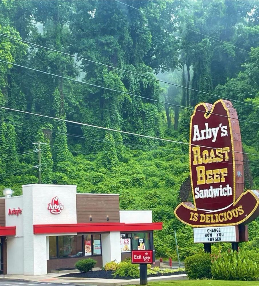 an arby’s in knoxville, tn with a lush green forested backdrop behind the big arby’s hat sign. majestic 