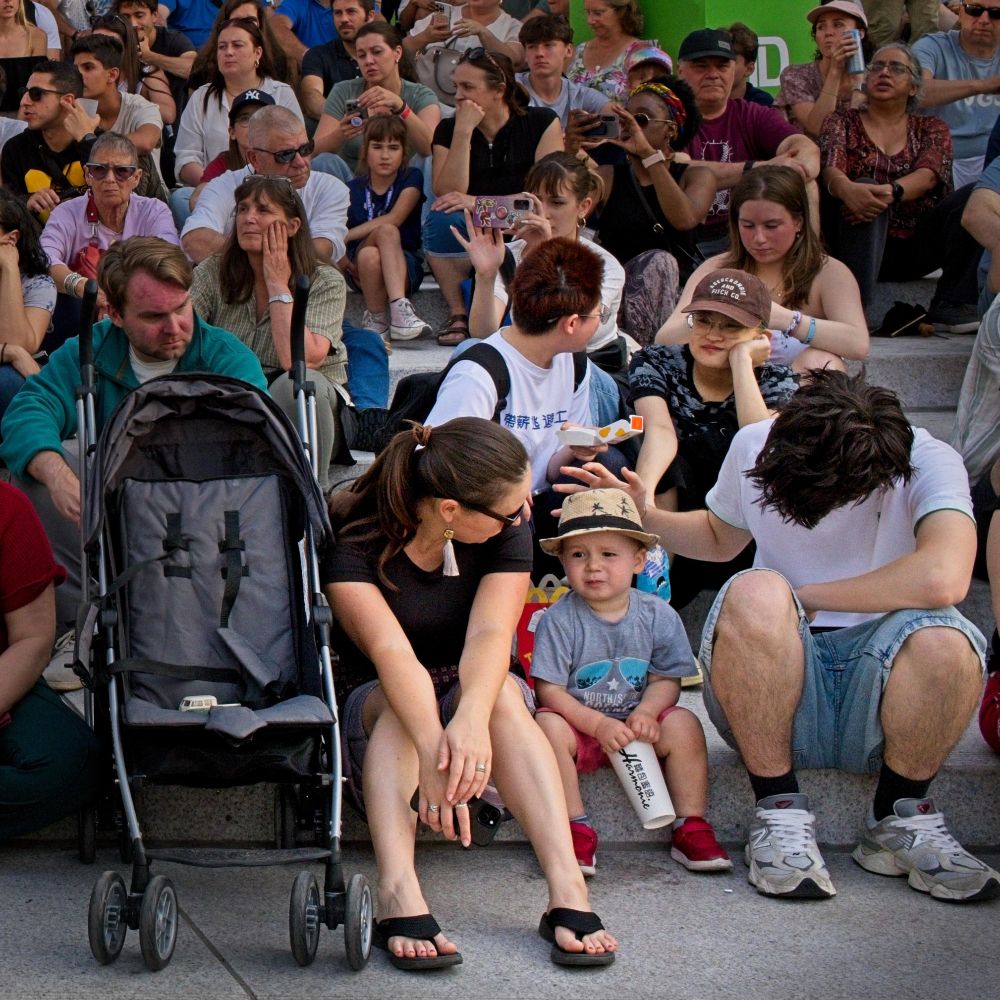 This is a photo of a crowd watching a show. There's a young boy, likely about two or three years-old, wearing a straw hat in the front row.