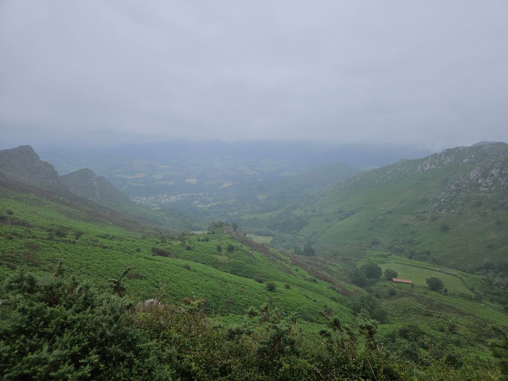 A green valley is spread between rocky foothills, half shrouded in fog.