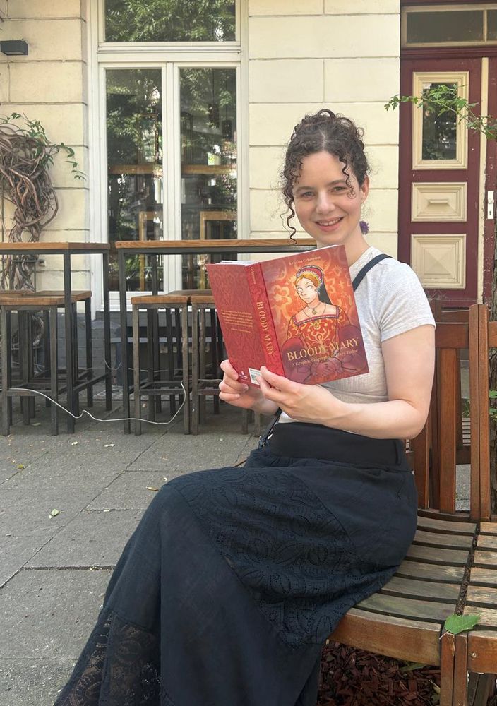 Me, sitting outside and holding a copy of my graphic novel "Bloody Mary: A Graphic Biography of Mary Tudor".