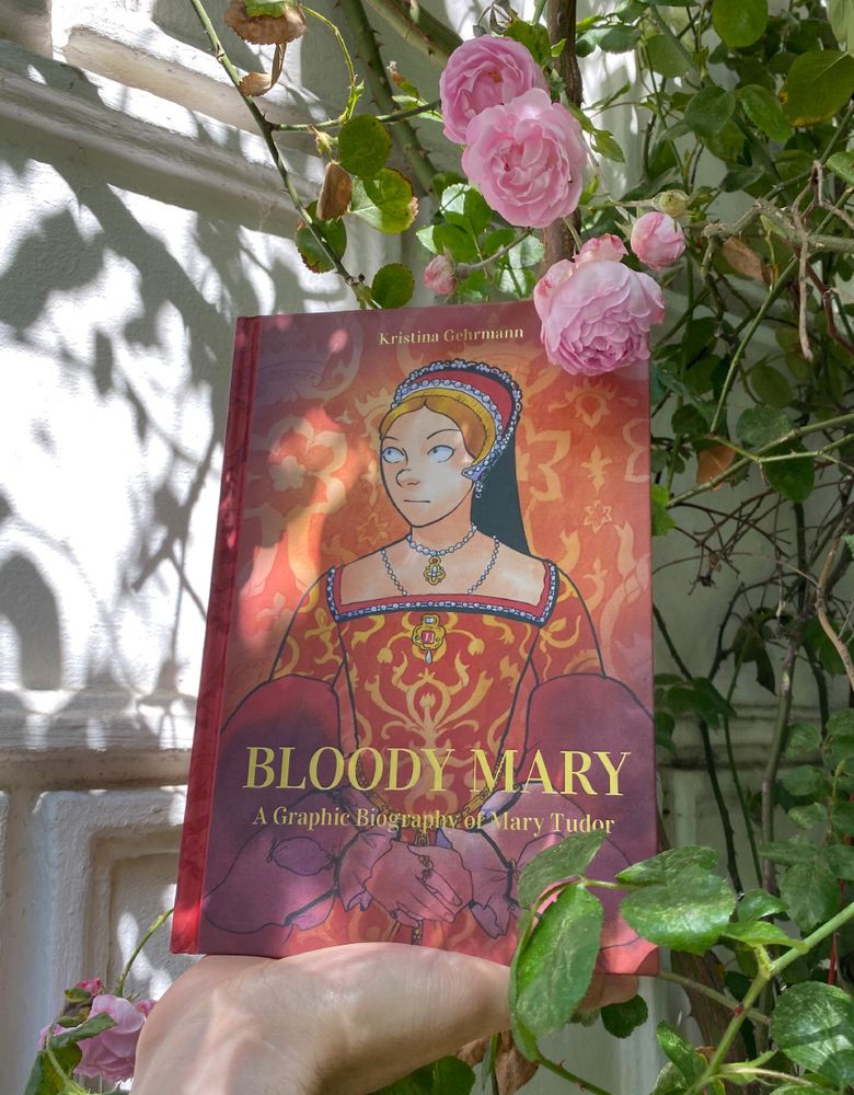 A copy of my graphic novel "Bloody Mary" being held in front of a rose bush.