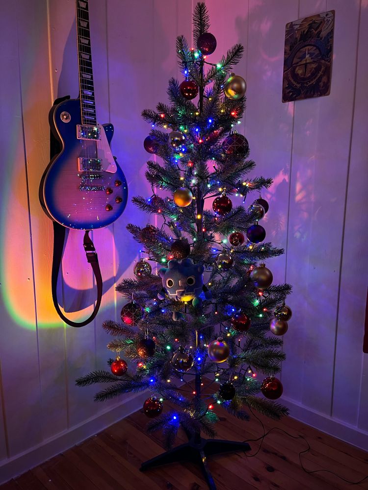 A godot plushie sitting in a christmas tree next to a guitar.