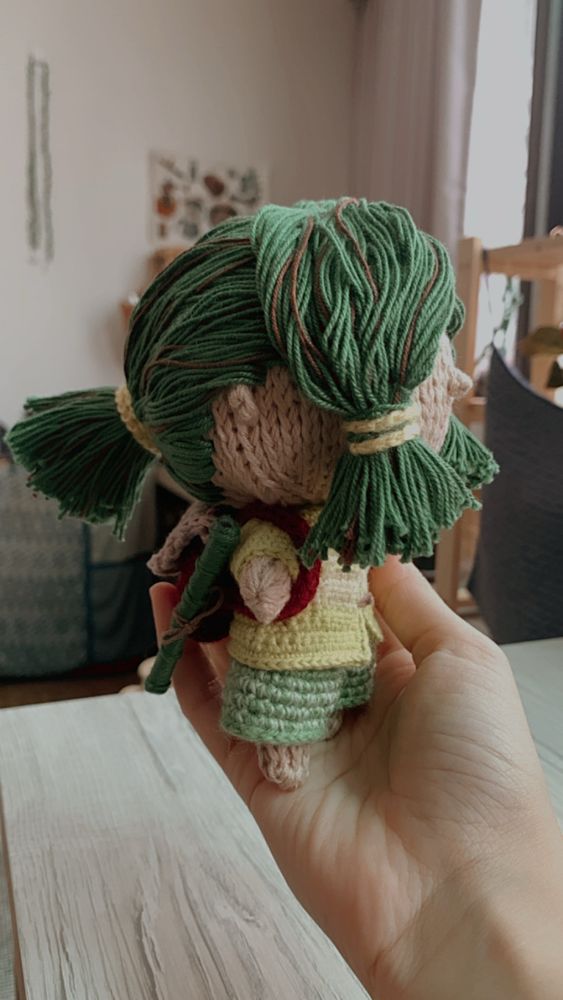 A handmade Tunisian crochet doll created based on the customer’s original character design. The doll has green hair styled in a ponytail, a green outfit, and a red backpack.