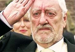 a man with a beard wearing a suit and tie is saluting with his hand on his forehead .