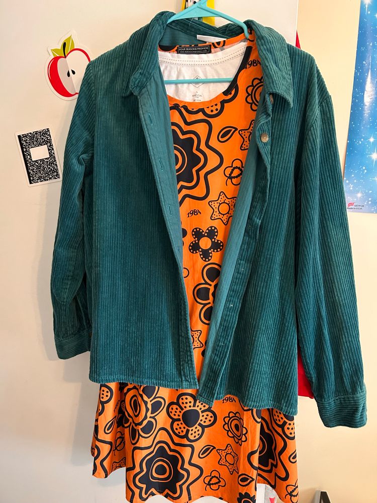 A photo of an orange dress and teal corduroy jacket on a hanger.