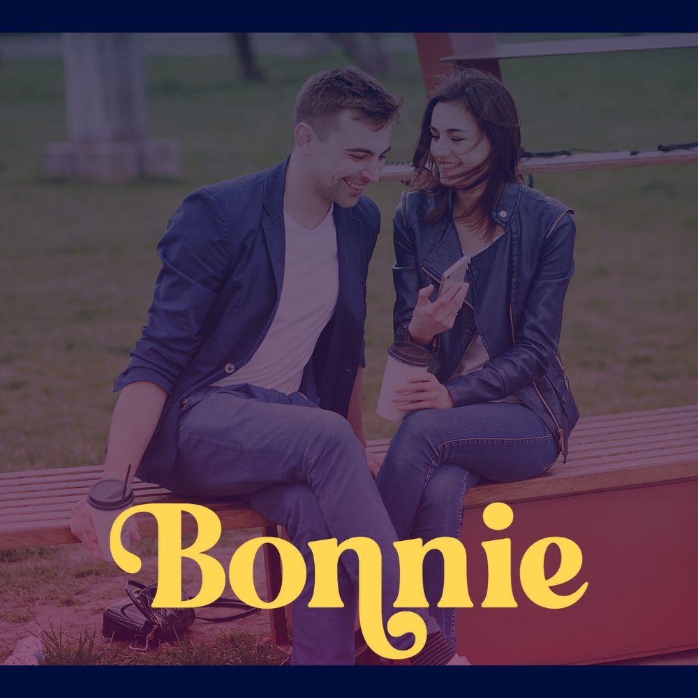 Man and woman sitting on park bench looking at a phone and smiling