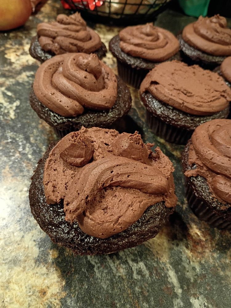 Chocolate cupcakes. The frosting looks like the poo emoji on most of them. The foremost cupcake has a sad face in frosting.