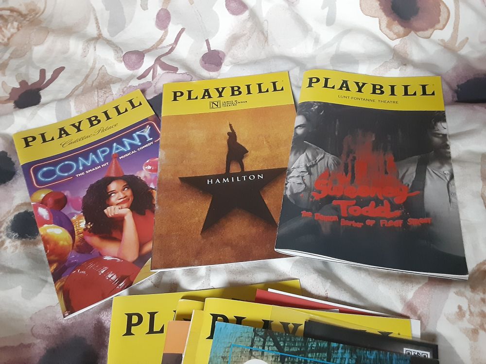 Some playbills lying on my bed. There is Company, Hamilton, and Sweeney Todd with a small pile of others below them.
