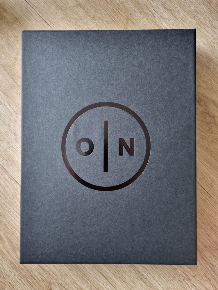 Front cover of ON game journal black case. Symbol is a black circle with the letters O and M separated by a vertical line. 