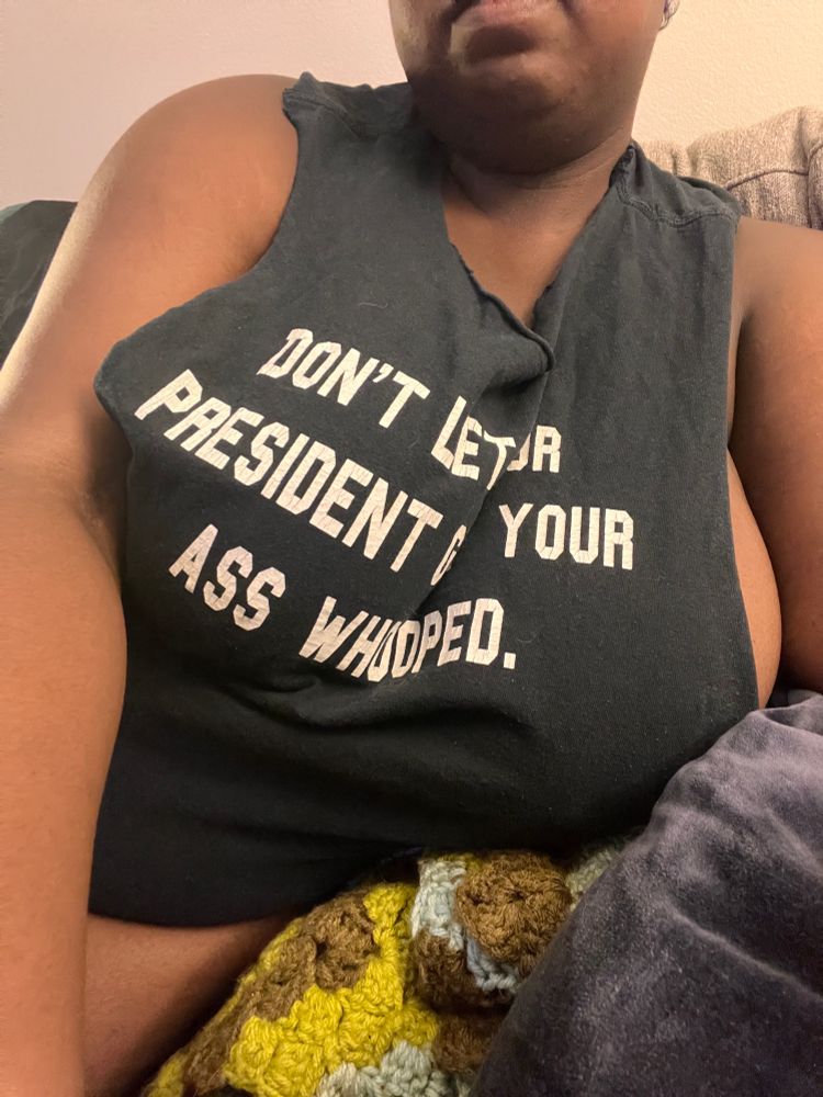 Image of me, wearing a black t shirt that I cut the sleeves and neck off of. It has white text that reads “Don’t let your president get your ass whooped”