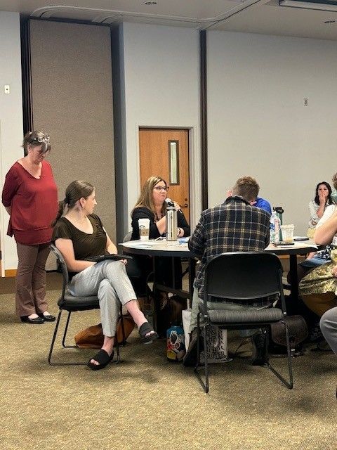 Participants sitting at table- one holding microphone giving feedback to presenter.