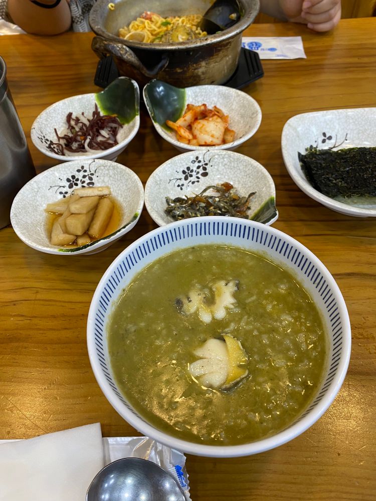 手前はアワビの浮かんだアワビ粥、副菜4〜5皿を挟んで奥にアワビラーメン