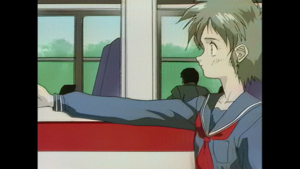 A screenshot from an anime (Key The Metal Idol) that depicts a young girl right next to a moving train who is reaching forward in the direction the train is moving with a somewhat robotic pose and no emotion on her face. She is wearing a blue sailor uniform.