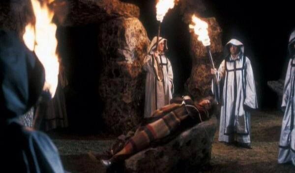 The Fourth Doctor is tied to a sacrificial stone while druids encircle him with torches, in a Stonehenge semblance under the night sky.