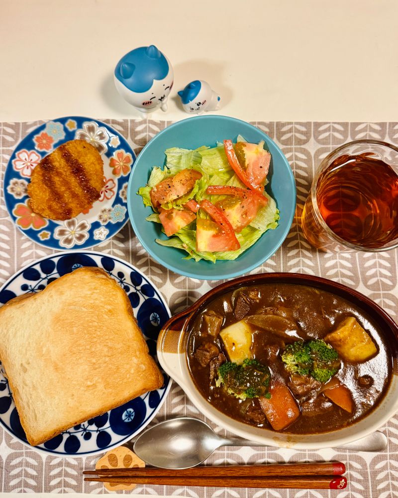 ビーフシチュー、パン、サラダ、コロッケ、麦茶が並んだ食卓