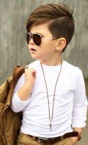 A cool kid wearing white shirt, aviators, holding jacket behind shoulder by hooking it on his finger. 