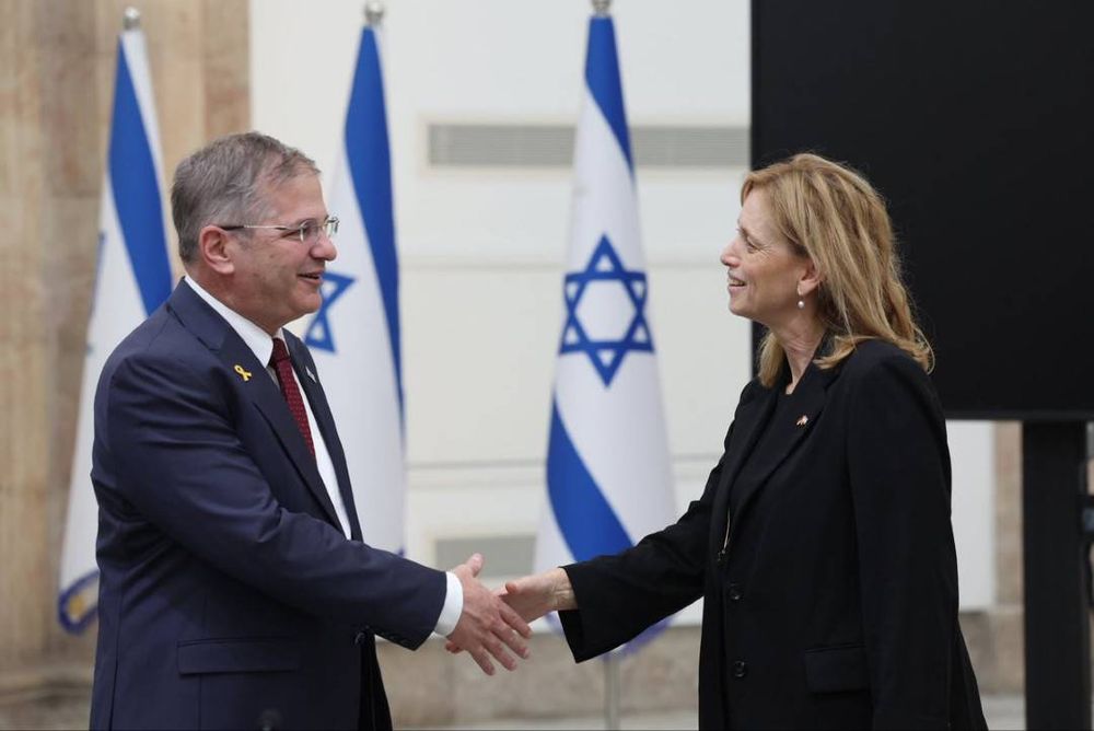 Karin Prien (weit rechts) nur Millisekunden vor einem Händedruck mit Yoav Kisch (womöglich noch weiter rechts, aber im Bild links). Im Hintergrund drei Flaggenkegel mit israelischen Flaggen.