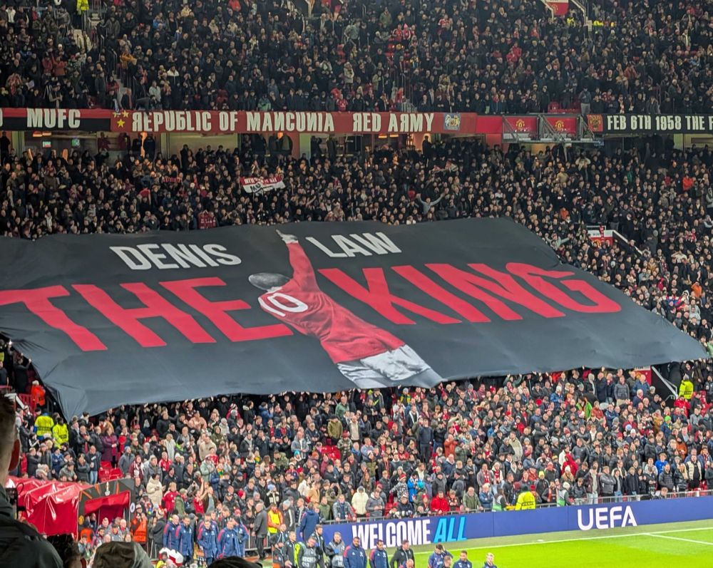 Large flag over supporters at Old Trafford behind the home goal remembering Denis Law The King of the Stretford End. 