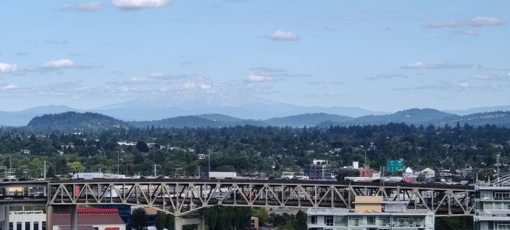 A photo of East Portland taken from West Portland, zoomed in on Mt. Hood, partially obscured by clouds