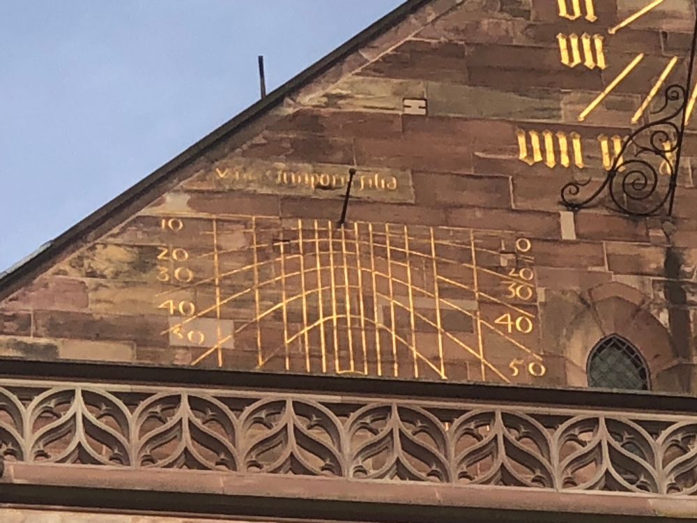 A different wall sundial with golden lines. Vertical parallel lines, not numbered, and a set of curved lines numbered 10-50 every ten.