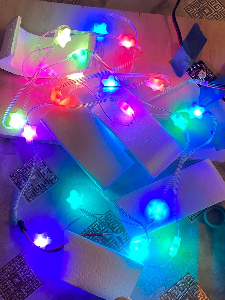 Star-shaped LED’s on a strand. They are lit in rainbow colors. The colors reflect off a pile of white styrofoam pieces carved into curves. 