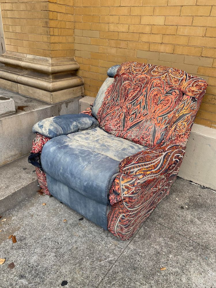 A shabby, cushioned chair with a half-complete cover made of sequined paisley fabric. 