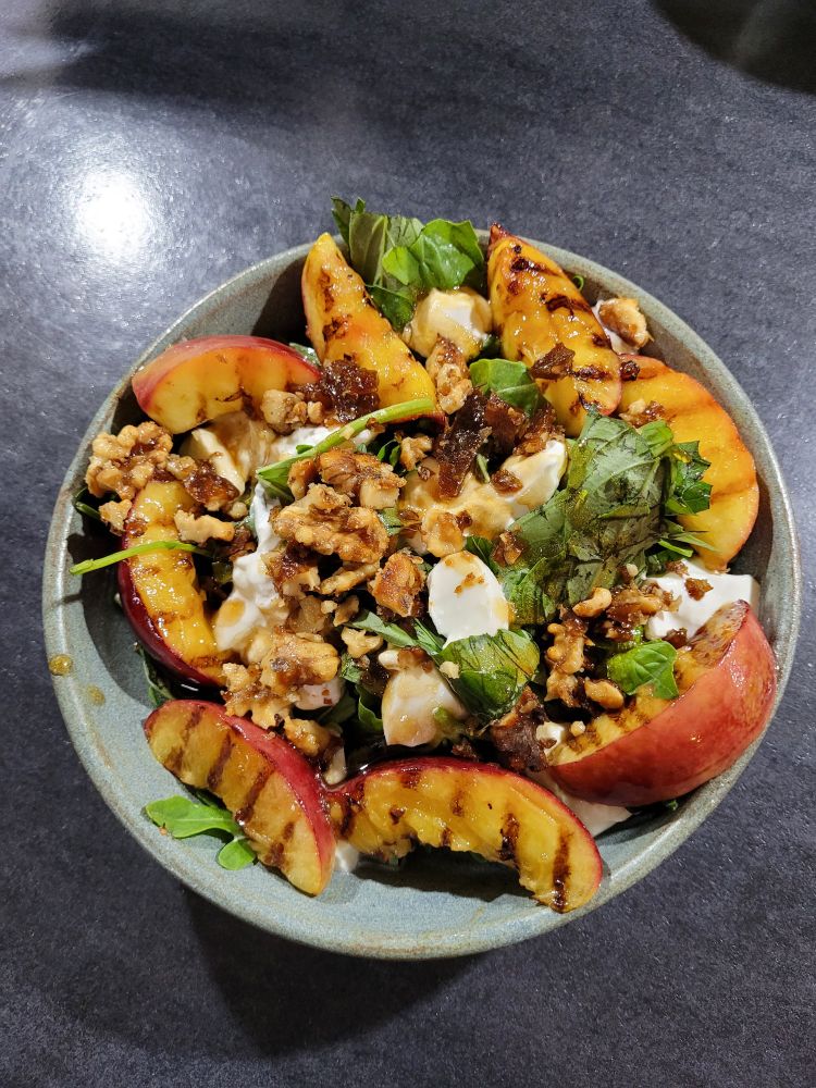 A green salad bowl filled with mixed leaves, chargrilled nectarines, burrata and candied walnuts