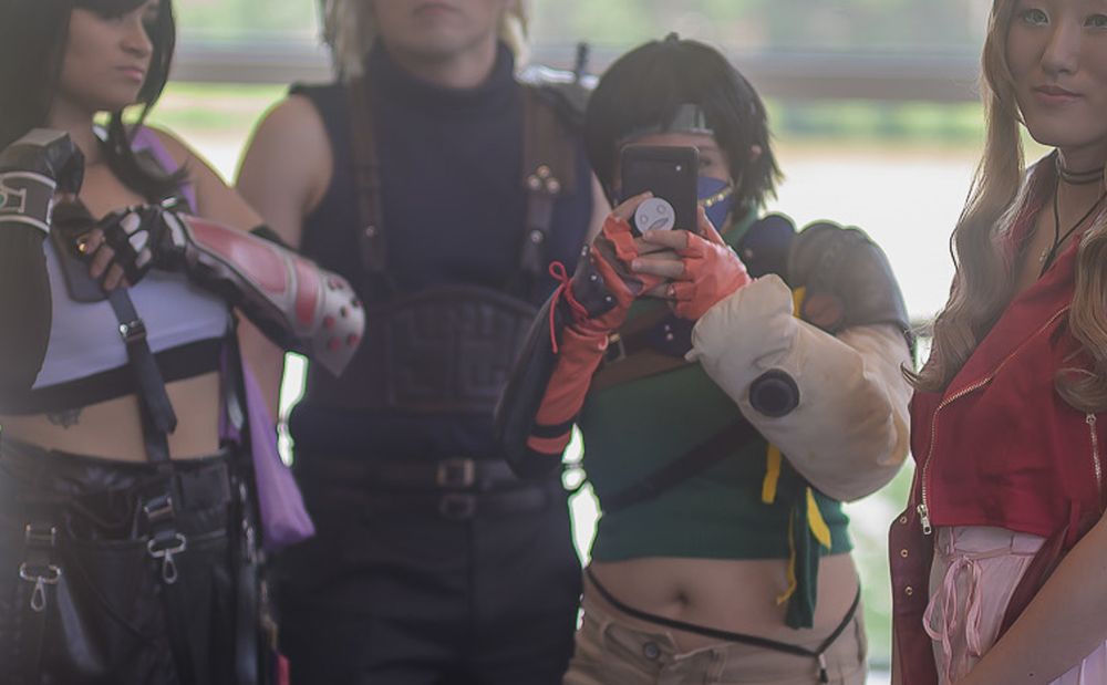 me cosplaying as Yuffie alongside friends cosplaying as Tifa, Cloud and Aerith from Final Fantasy 7, at Tekko 2025, but my phone is in front of my face because I'm taking a photo of Joe/L-Dragon Photography who is taking this photo. You can clearly see my Emil from NieR popsocket on the back of my phone, hehehe. The popsocket was designed by cephalxin from Singapore.