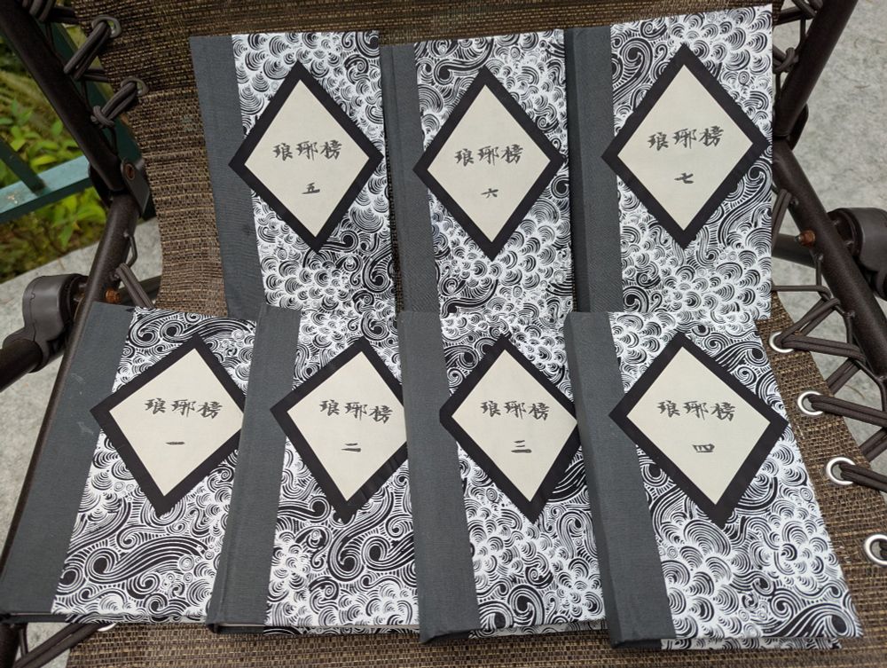 Seven books lying on a deck chair. They're titled 琅琊榜 volumes 1-7. They are black and white with wind patterned covers and grey spines. 