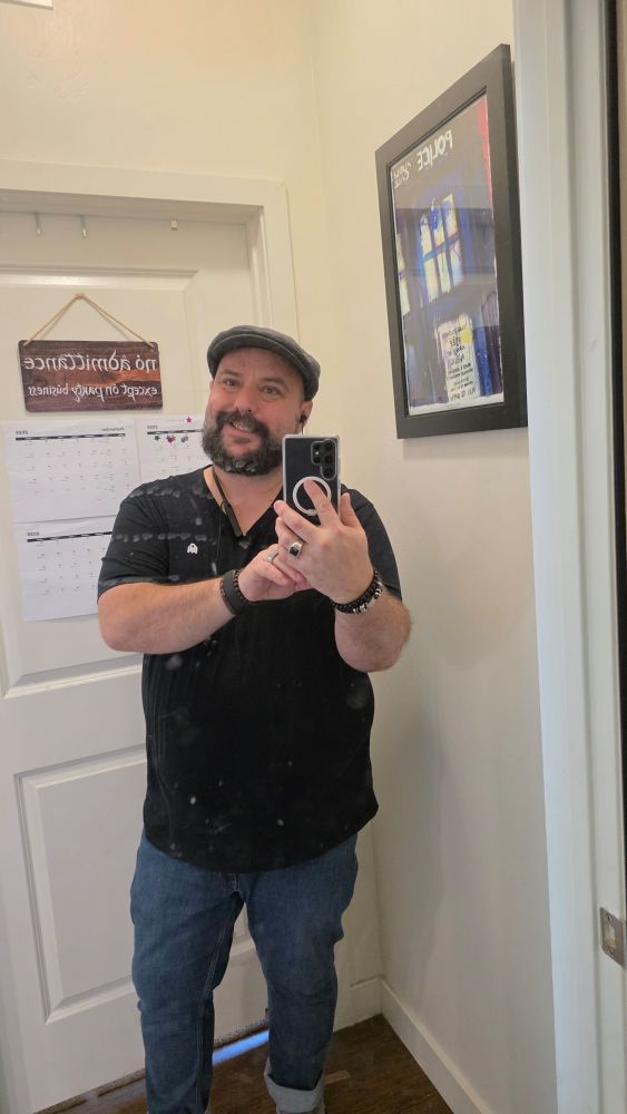 Nick in a black v neck & jeans smiles at the camera.